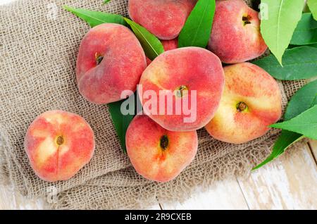 Fresh Flat Peaches, Chinese Saturn Donut Peaches with Leaves on Bright Background Stock Photo