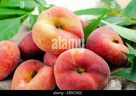 Fresh Flat Peaches, Chinese Saturn Donut Peaches with Leaves on Bright Background Stock Photo