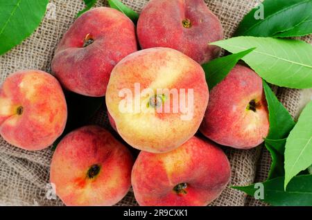 Fresh Flat Peaches, Chinese Saturn Donut Peaches with Leaves on Bright Background Stock Photo