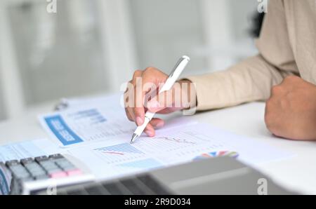 A person pointing at graph data with a pen on the desk with a calculator and laptop. Stock Photo