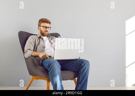 Handsome young bearded businessman sitting on chair in a empty space with laptop and working. Stock Photo