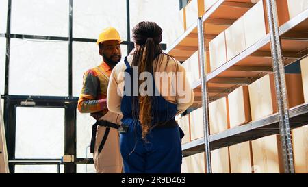 Group of workers scanning products in warehouse, using scanner and tablet to check barcodes for stock inventory. Man and woman working on logistics, cargo packs on racks and shelves. Handheld shot. Stock Photo