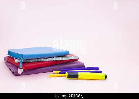Stack of notepads with pen and marker on pink table. Back to school. Copy space Stock Photo
