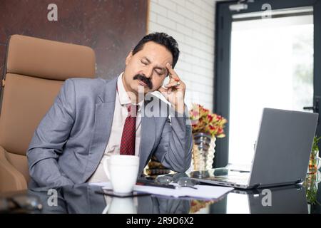 Mature indian businessman thinking of something while sitting in office Stock Photo