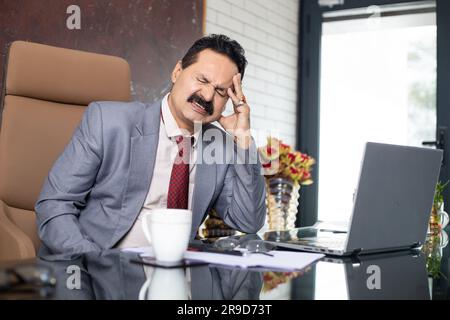 Mature indian businessman having a headache after working long hours in office. Workload Concept. Stock Photo