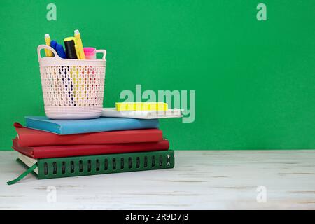 Stack of notepads with pencil case of markers on white table. Green board. Back to school. Copy space Stock Photo