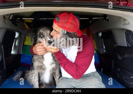 Gay man sitting inside a van with his black pet dog enjoying the sunny day. Stock Photo