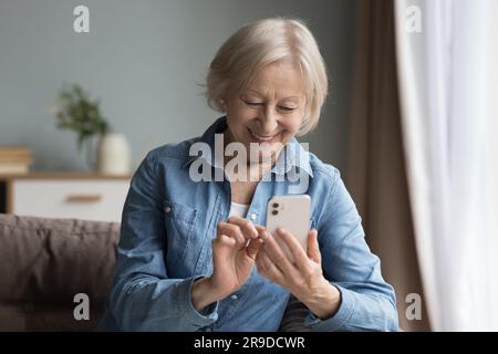 Smiling elderly woman using cell phone seated on couch Stock Photo