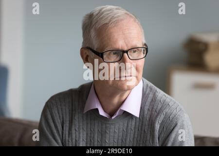 Concerned serious mature man in glasses sit on sofa indoors Stock Photo