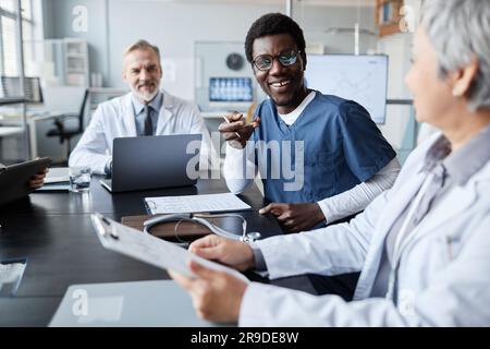 Happy young African American assistant in uniform looking at mature female colleague sitting next to him during discussion of working points Stock Photo