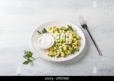 Turkish scrambled eggs with zucchini served with yogurt on a light blue background. Delicious homemade vegetarian food. Stock Photo