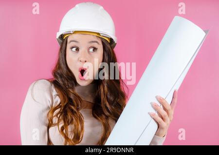 Portrait young woman architect with long hair looking excited holding her project in her hands on the pink background Stock Photo