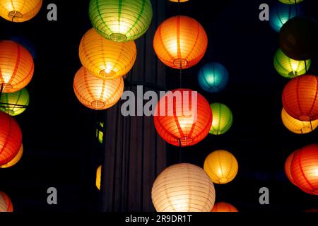 Many round Chinese paper lanterns hanging in the dark. A lot of festive colorful decorations prepared for a celebration in an oriental style Stock Photo