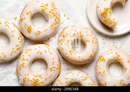 Homemade baked iced donuts with golden pearls on a white plate and on baking paper. Stock Photo