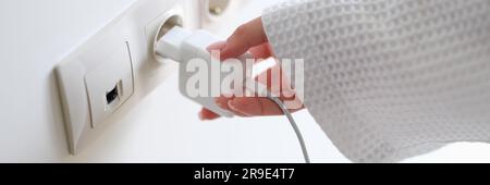 Woman in white bathrobe inserting plug into outlet at home with hand closeup Stock Photo