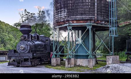 Cass, West Virginia, June 18, 2022 - View of an Antique Shay Steam Engine Warming Up by an Old Water Tower Blowing Smoke Stock Photo