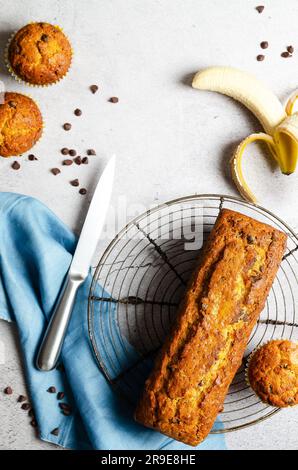 A banana bread with chocolate chips, some muffins, a banana and a blue napkin, on grey background. Stock Photo