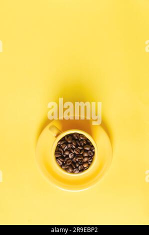 Coffee beans in yellow cup on yellow background, top view. Stock Photo