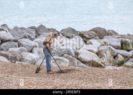 A man using a metal detector on a shingle beach Stock Photo