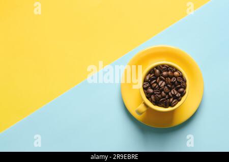 Coffee beans in yellow cup on blue and yellow background. Stock Photo