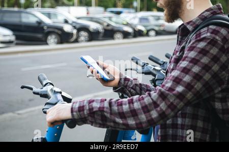 Close up of man hand using mobile app for rental electric scooter. Stock Photo