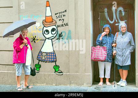 Glasgow, Scotland, UK 26th June, 2023. UK Weather:  Wet  in the city as George square sees tourists and locals suffer in the rain.Banksy exhibition tribute with the duke in a kilt and the cone as canadian tourists cannot hide their bemusement. Credit Gerard Ferry/Alamy Live News Stock Photo