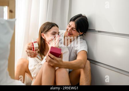 Handsome man holding small red box with gift to amazed girlfriend Stock Photo