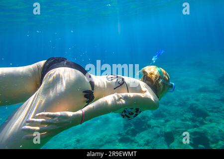 Female apnea bikini swims in crystal sea. Underwater background of a woman snorkeling and doing free diving. Watersport activity in summer vacations Stock Photo
