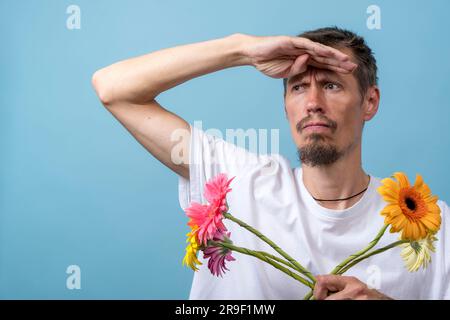 Portrait of a cute Caucasian thoughtful guy with a bouquet of flowers in his hands, who waits and looks into the distance with his palm to his forehea Stock Photo