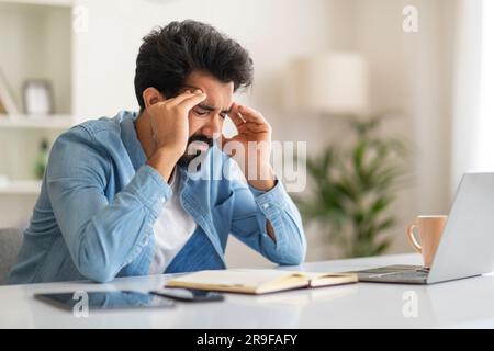 Stressed Young Indian Male Freelancer Having Headache While Working In Home Office Stock Photo