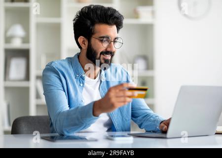 Online Payments Concept. Handsome Indian Man Using Laptop And Credit Card Stock Photo