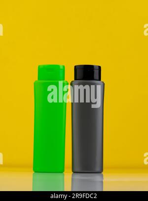 Two clear plastic bottles, one green and one black, set against a bright yellow background Stock Photo
