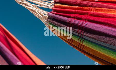 Close-up image of two rainbow colored hammocks against the blue sky Stock Photo