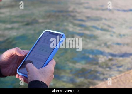 Female hand holding smartphone against sea background. Stock Photo