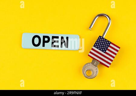 On a yellow surface, an open lock with the image of the US flag with a key and a sticker with the inscription - open Stock Photo