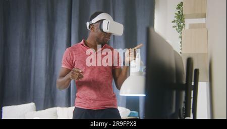African American man emotional talks and gesticulates on online conference using VR headset. Gamer plays in augmented reality game at home. Concept of using high tech devices in work and everyday life Stock Photo