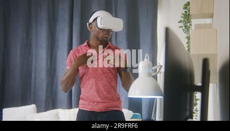 African American man emotional talks and gesticulates on online conference using VR headset. Gamer plays in augmented reality game at home. Concept of using high tech devices in work and everyday life Stock Photo