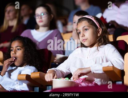 Preteen girl with african american friend watching movie in cinema Stock Photo
