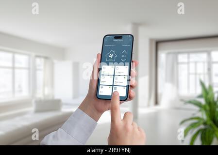 Person controls the temperature and lighting in the house with the help of an app on a mobile phone. A modern smart home application with the most imp Stock Photo