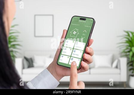 Woman use smart home app on smart phone. Living room interior in background. Home automation concept Stock Photo