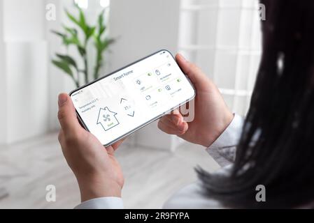 Modern living as a woman effortlessly manages her smart home using a mobile phone, living room backdrop Stock Photo