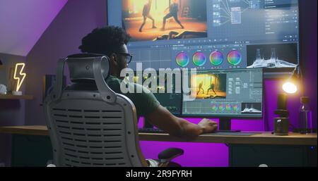 African American editor makes color correction, edits action movie, works at home. Software interface with RGB tools and wheels on computer and big digital screen. Concept of film post production. Stock Photo