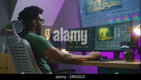 African American video maker edits action movie, makes color grading, works at home. Software interface with RGB tools and wheels on computer and big digital screen. Concept of film post production. Stock Photo