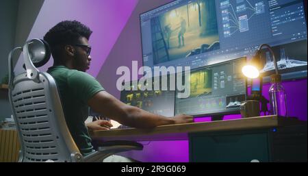 African American video editor makes color grading, works at home office. Computer and big digital screen with program interface with RGB tools and action movie footage. Film post production concept. Stock Photo