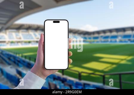 Mockup of phone in hand in modern stadium. Isolated screen for adding an app or website. Empty stadium with seats and grass in background Stock Photo