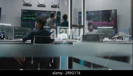 Multi ethnic team of traders work on multi-monitor computers with displayed real-time stocks. Colleagues analyze exchange market charts on multiple big screens. Cryptocurrency trading and investment. Stock Photo
