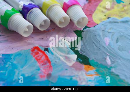 Tubes of colored paint against the background of a bright multi-colored palette of the artist close-up. Stock Photo