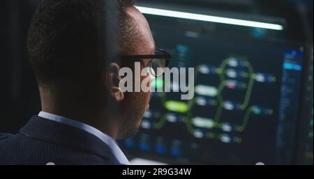 African American software engineer looks at computer screen with displayed big data server and blockchain network, monitors real-time analysis charts in monitoring office. Concept of cyber security. Stock Photo