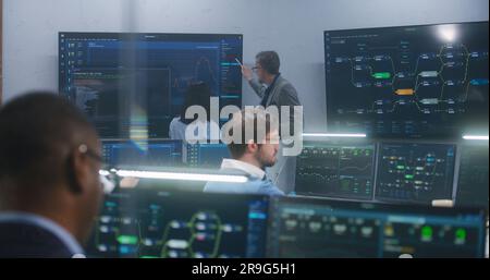 Technical support specialists sit at computers with displayed blockchain network map and server data. Big data scientists work in monitoring room. Big screens on the wall. Concept of cyber security. Stock Photo