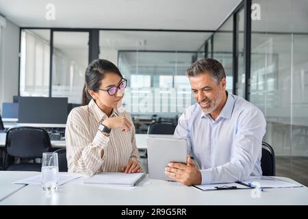 Two busy diverse executives team discussing work using digital tablet in office. Stock Photo
